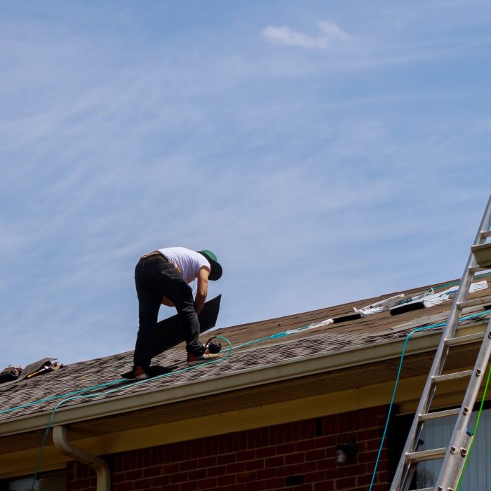 Roof repair, worker with replacing gray tiles shingles on house being applied